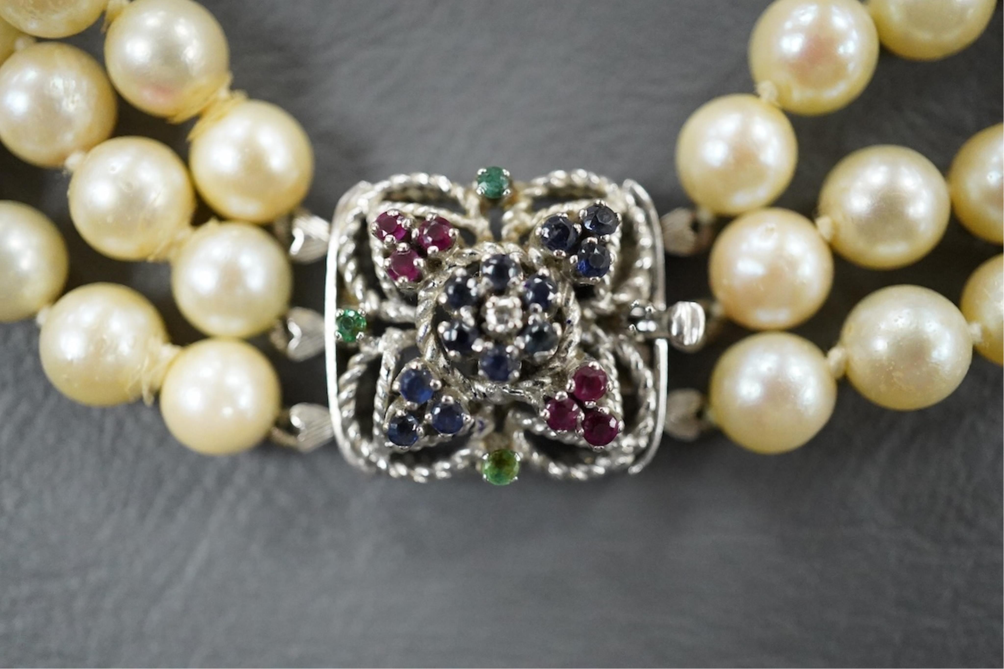 A triple strand cultured pearl necklace, with an Italian 18k white metal, ruby, sapphire and emerald set clasp, 46cm.
